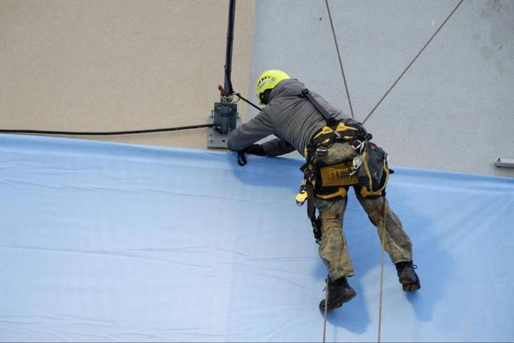 Técnico realizando manutenção em altura, usando equipamento de segurança para trabalhar em uma fachada de edifício